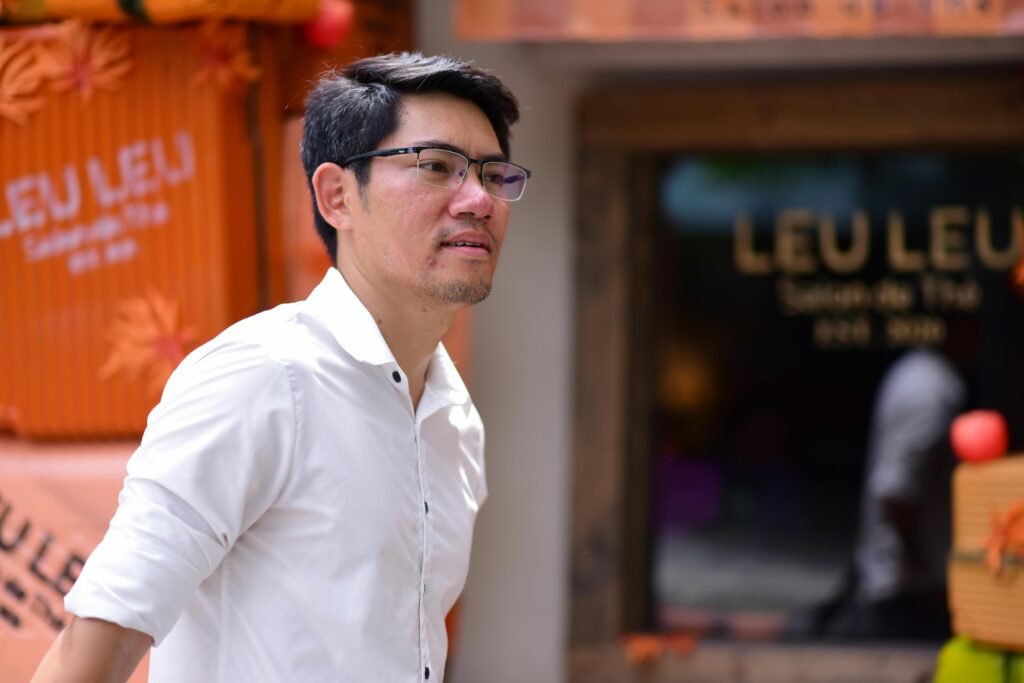 A man wearing glasses and a white shirt walking past a colorful cafe with autumn decorations.
