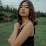Elegant portrait of a young woman posing thoughtfully outdoors in a lush green setting.